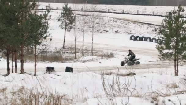 El tipo está montando un ATV en un camino cubierto de nieve en invierno — Vídeos de Stock