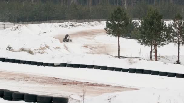 El tipo está montando un ATV en un camino cubierto de nieve en invierno — Vídeo de stock