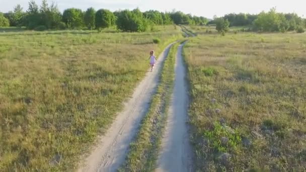 Liten flicka i en vit sundress med rött mönster kör över fältet — Stockvideo