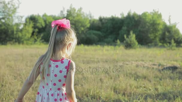 Petite fille dans une robe de soleil blanche avec des motifs rouges courant à travers le champ — Video