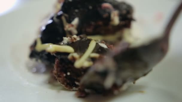 Hand with a spoon breaks off a piece of chocolate cake on a plate — Stock Video