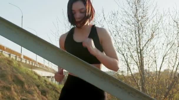 Jeune jolie sportive est engagée dans la remise en forme dans la nature. La jeune fille fait des exercices à l'extérieur de la ville. Steadicam shot — Video