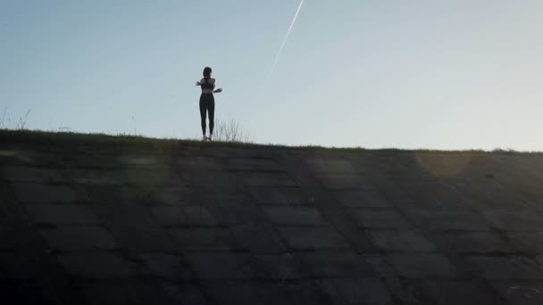 Unga vackra idrottskvinna bedriver fitness i naturen. Flickan utför övningar utanför staden. Steadicam skott — Stockvideo