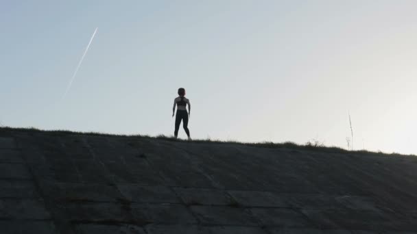 Young pretty sportswoman is engaged in fitness in nature. The girl performs exercises outside the city. Steadicam shot — Stock Video