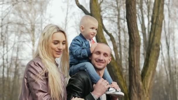 Счастливая семья из трех человек гуляет по весеннему парку — стоковое видео
