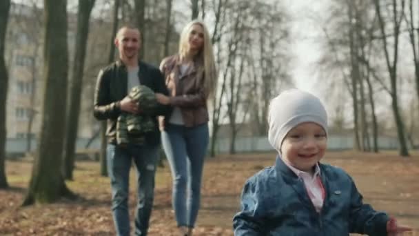 Счастливая семья из трех человек гуляет по весеннему парку — стоковое видео