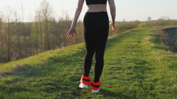 Юная симпатичная спортсменка занимается фитнесом на природе. Девушка выполняет упражнения за пределами города. Стедикам-шот — стоковое видео