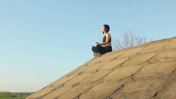 Joven chica bonita se dedica a la meditación sentado en losas de hormigón . — Vídeo de stock