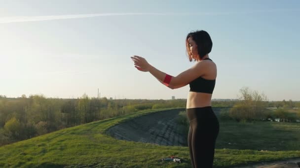 Ung söt tjej gör gymnastik vid solnedgången. Idrottaren utför övningar med en fitness gummiband — Stockvideo