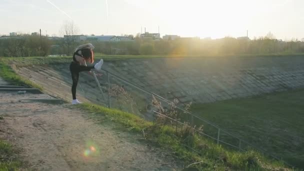 Симпатичная молодая девушка делает растяжку на заднем плане заходящего солнца — стоковое видео