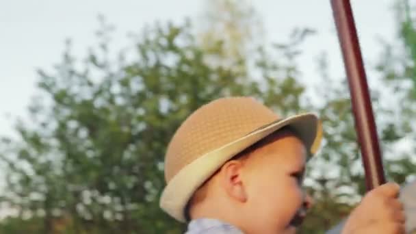 Gladlynt pojke 2-3 år i en hatt som rider en gunga — Stockvideo