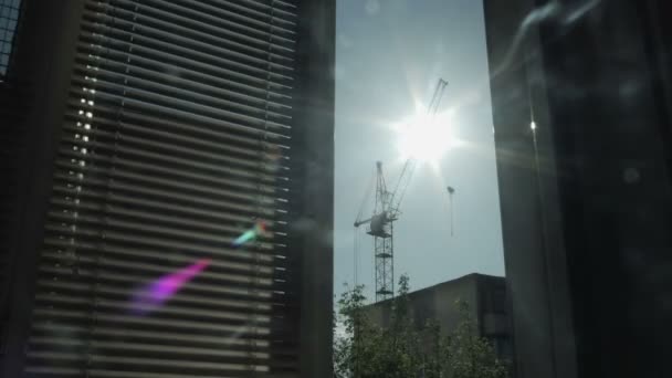 Slunce se pohybuje proti siluety domů a stavební věžový jeřáb. Pohled z okna — Stock video