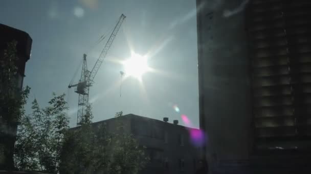 太陽は、住宅と建設のタワー クレーンのシルエットに対して移動します。窓からの眺め — ストック動画