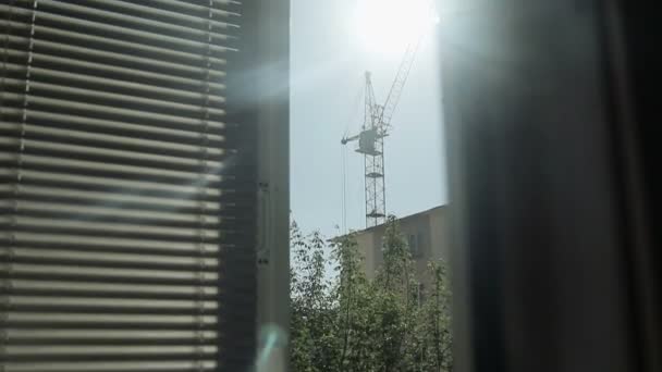 Pohled z okna na siluetu budovy věž jeřábu a domy — Stock video