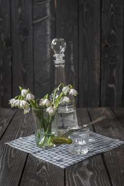 Bir bardak votka, salatalık turşusu ve çatalla cam sürahide ve koyu ahşap arka planda.