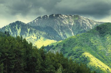 Kimasar Gorge Almatı, Kazakistan, Zailiysky Alatau Sıradağları 'nın yamaçlarında güneş ışınları olan fırtınalı bir gökyüzünün arka planında Kumbel Tepesi, 