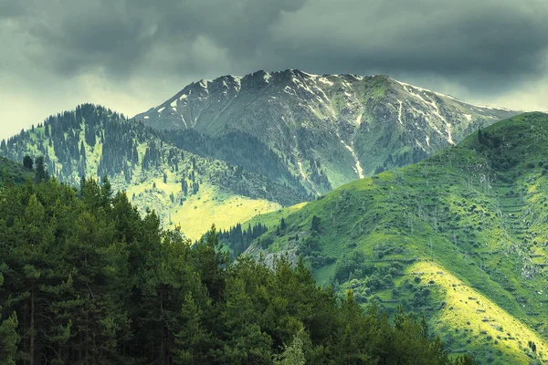 Kimasar Gorge Almatı, Kazakistan, Zailiysky Alatau Sıradağları 'nın yamaçlarında güneş ışınları olan fırtınalı bir gökyüzünün arka planında Kumbel Tepesi, 