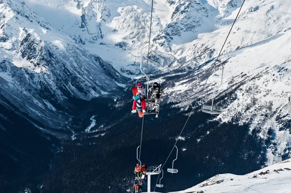 Skifahrer und Snowboarder mit der Sesselbahn ins Skigebiet hoch in den winterlichen Schneebergen — Stockfoto