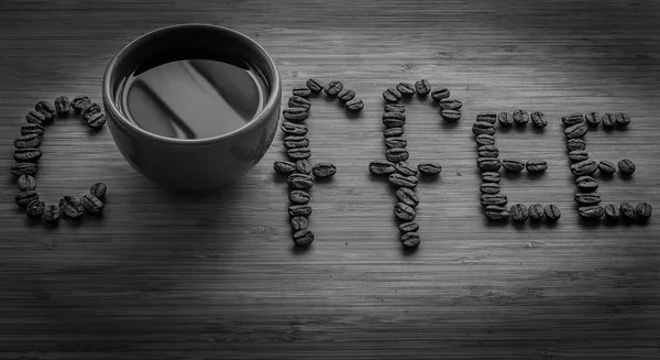 Coffee letters made of beans and cup on vintage boards. Black and white picture — Stock Photo, Image