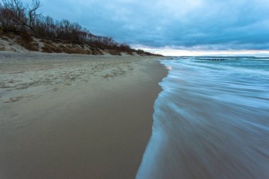 Kumlu sahil ve denizde gelgit. Mavi alacakaranlıkta bulutlu havada uzun süre açık havada.