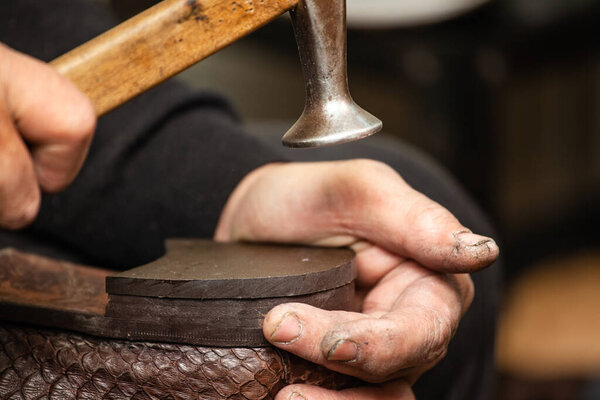 close-up of hands male shoemaker repairing shoes by nailing a heel