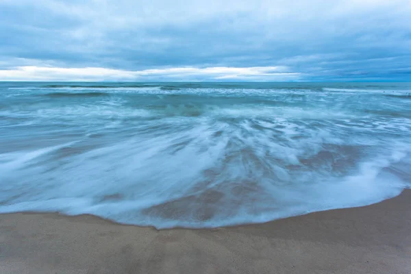 長い露出の上に曇りの天気で青い夕暮れ時に砂浜で波と潮 — ストック写真