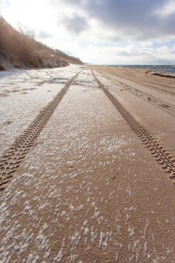 Karla kaplı bir plajın kumlarında lastik izleri var.