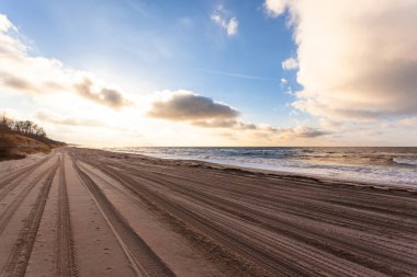 Deniz kenarındaki geniş plajda lastik izleri var.