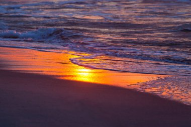 Sörf çizgisindeki turuncu günbatımı güneşinin parlak yansıması
