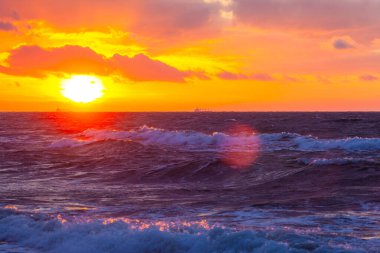 Gün batımında bulutlu bir gökyüzünde parlak turuncu güneş.