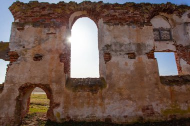 Eski bir ortaçağ kırmızı tuğla binasının yıkıntıları arasında kemerli pencereleri ve girişi olan yıkılmış bir duvar.