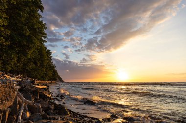 Vahşi kayalıklarda, denizin üzerinde parlak turuncu gün batımı