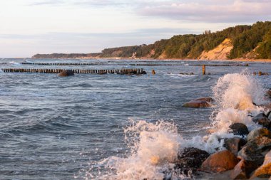Deniz dalgaları yaz günbatımında sahilde kayalara çarpıyor.