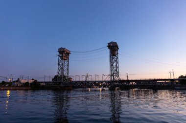 Alacakaranlıkta iki uzun kuleli büyük demir köprü.