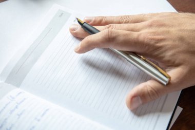 Günlük sayfasının üzerinde dolmakalem olan bir elin yakın plan görüntüsü
