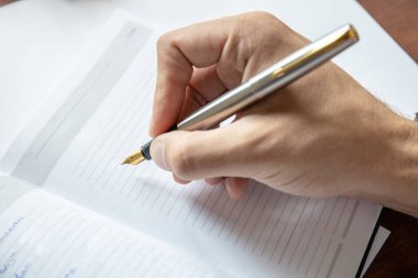 Günlük sayfasının üzerinde dolmakalem olan bir elin yakın plan görüntüsü