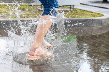 Su birikintisinde zıplayan bir kızın bacakları.