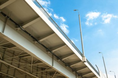 Açık mavi gökyüzünün altında sokak lambaları olan modern bir otomobil köprüsünün yapısı