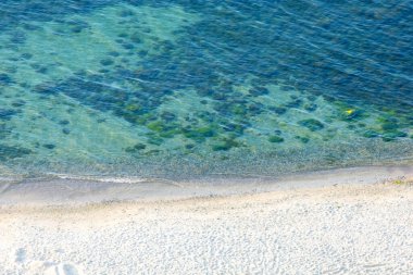 Kumlu sahili ve mavi suyu olan deniz manzarası.