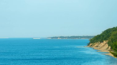 açık güneşli bir gökyüzünün altında, mavi denizin dik, ağaçlık kıyılarının resimsel manzarası.