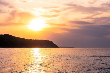 Arka planda uçurum olan resim gibi deniz kıyıları, mor ışıkta gün batımında alçak güneş.