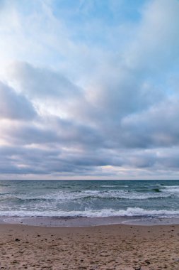 Turkuaz deniz kıyısındaki kumlu sahil. Gün batımında bulutlu bir havada.