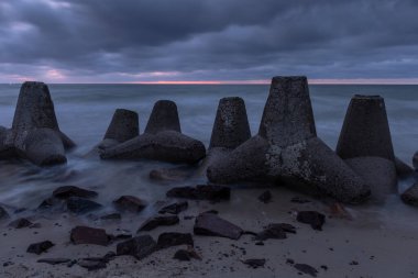 Deniz kıyısının dramatik kasvetli manzarası, kumsalda beton dalgalanmaları, uzun süre açık havada karanlık, gri bulutlu bir gökyüzünün altında.