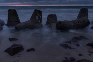 Deniz kıyısının dramatik kasvetli manzarası, kumsalda beton dalgalanmaları, uzun süre açık havada karanlık, gri bulutlu bir gökyüzünün altında.