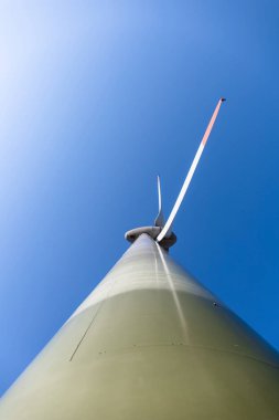Mavi gökyüzünün arka planında büyük pervaneleri olan rüzgar jeneratörü
