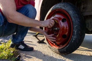 Şoför yolun ortasında yedek lastiği takıyor.