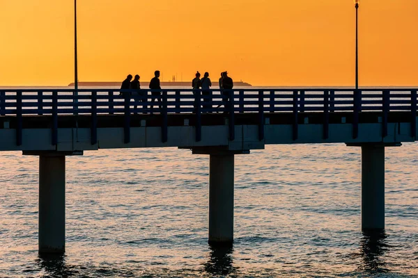 Sylwetki Ludzi Spacerujących Molo Nad Morzem Przed Zachodem Słońca Pomarańczowe — Zdjęcie stockowe