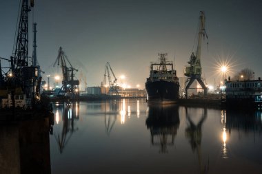 Nehirde büyük bir gemi ve vinçlerle gece limanı