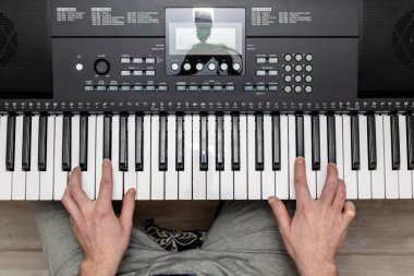 Parlak bir ev stüdyosunda sentezleyici çalan bir piyanistin elleri.