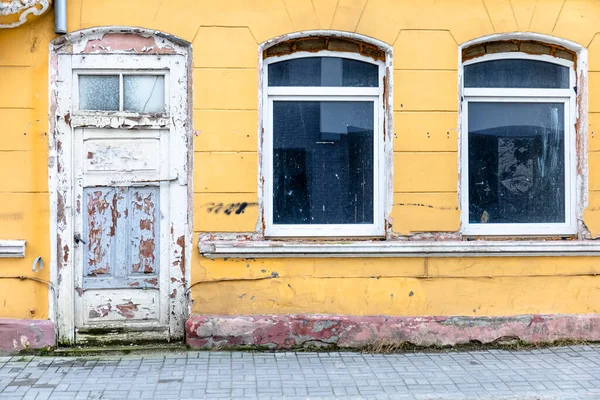 wall of an old building with yellow walls and a wooden door with peeling white paint